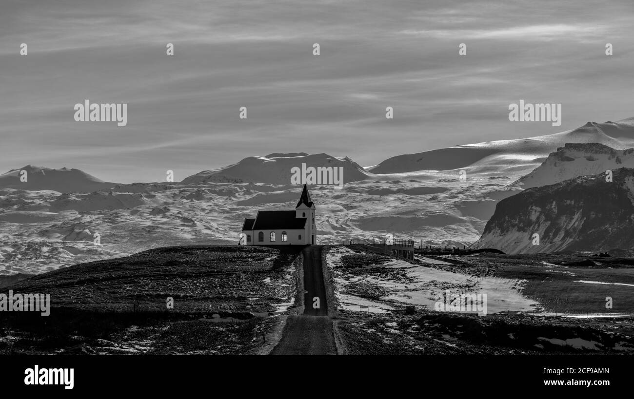 Foto in bianco e nero di una bella chiesa situata Vicino strada di campagna ruvida contro cielo nuvoloso in Islanda Foto Stock