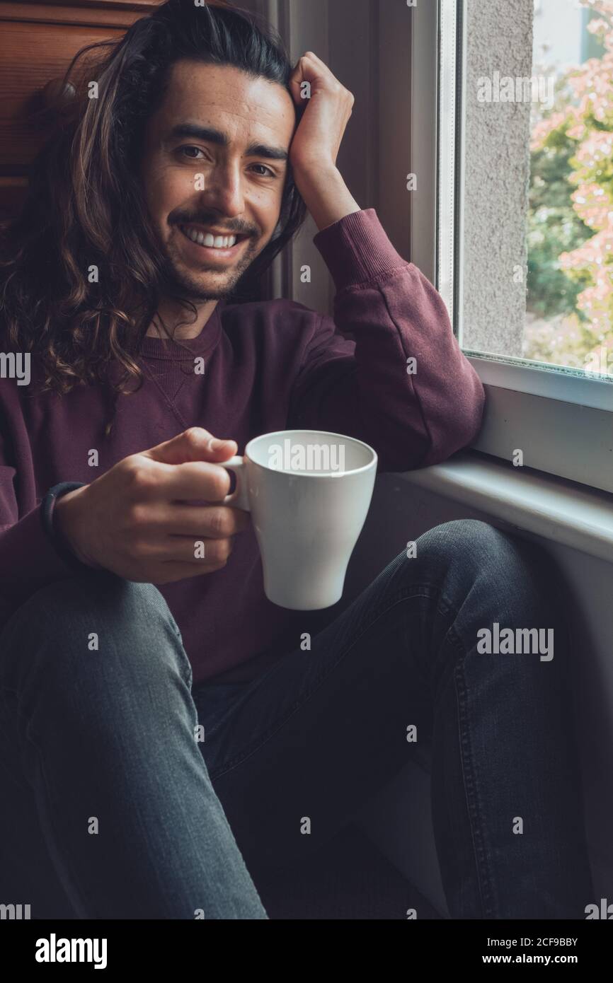 Adulto maschio con tazza che guarda fuori finestra Foto Stock