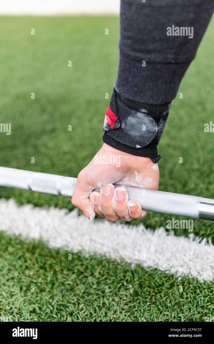 Crop mano di atletico maschio in gesso polvere che tiene barbell su erba Foto Stock
