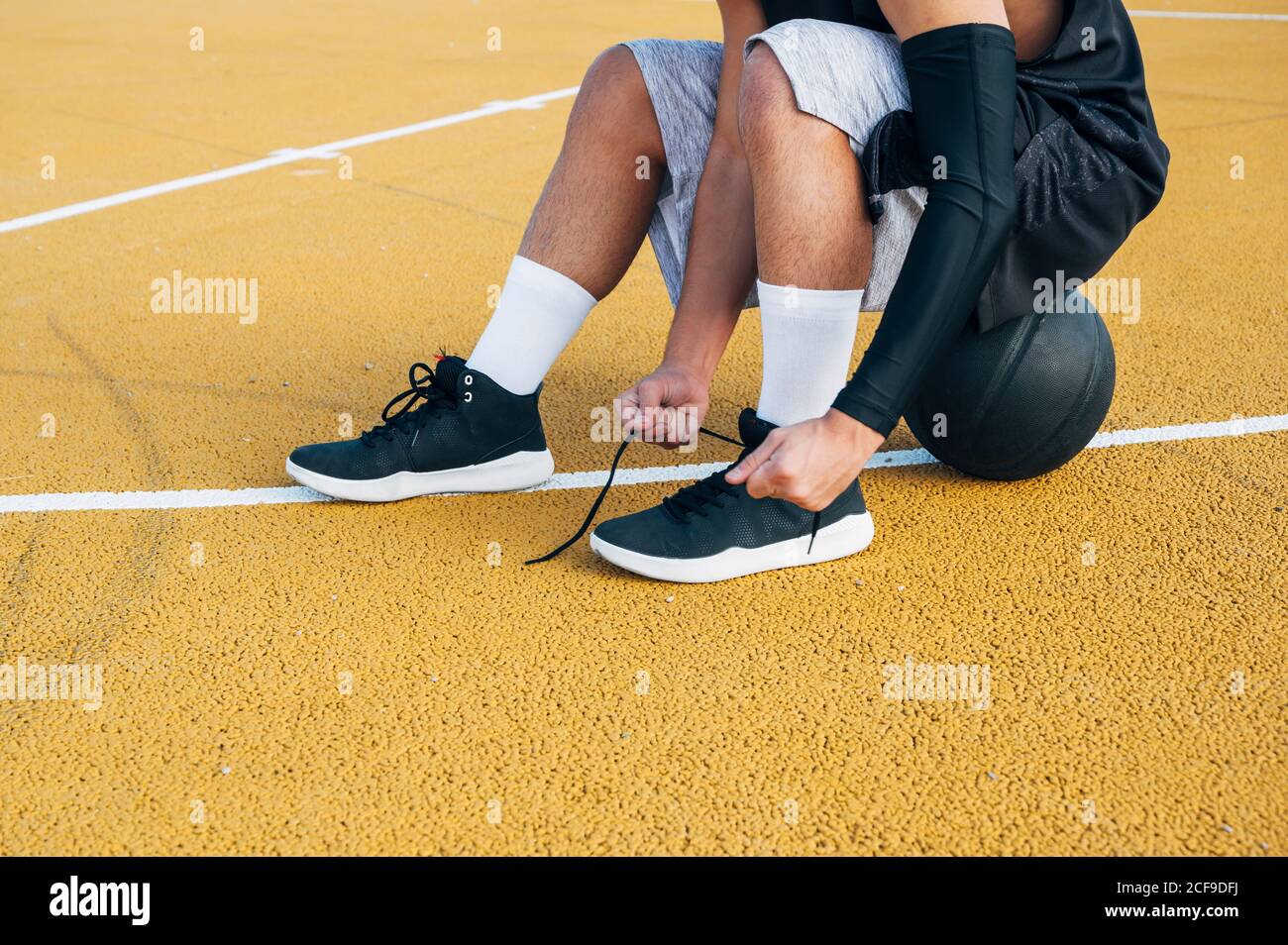 Gambe di raccolto giovane uomo e palla seduta sul basket corte all'aperto che fissa la sua calza Foto Stock