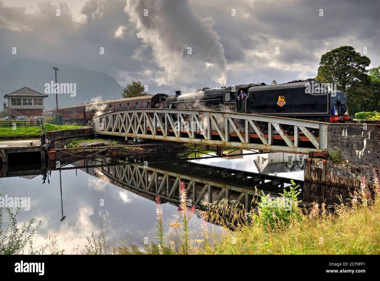 Il treno a vapore Jacobite che passa sopra il ponte di oscillazione della ferrovia di Banavie, sulla strada per Mallaig. (Elaborata come immagine HDR). Foto Stock