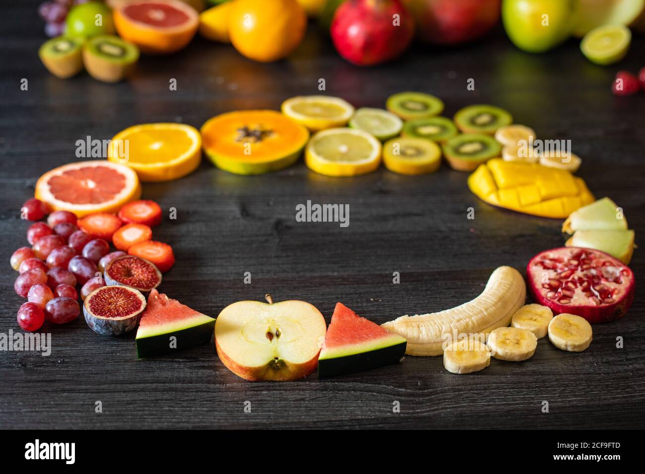 Dall'alto varie frutta e verdura sane sbucciate e tagliate disposto in cerchio su un tavolo di legno nero Foto Stock