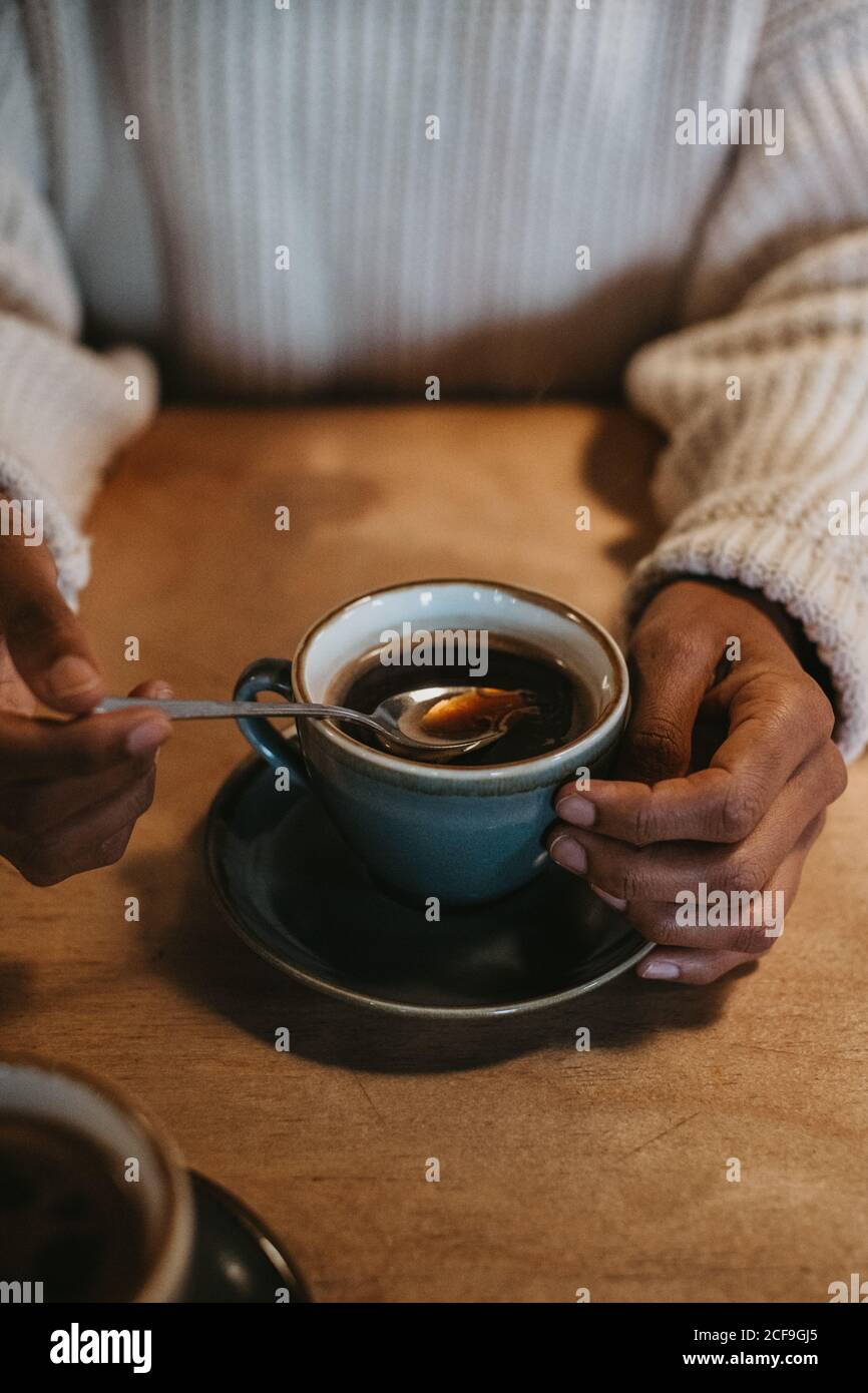 Da sopra raccolto mani di donna irriconoscibile seduta a legno tavolo con caffè caldo in tazza rustica Foto Stock