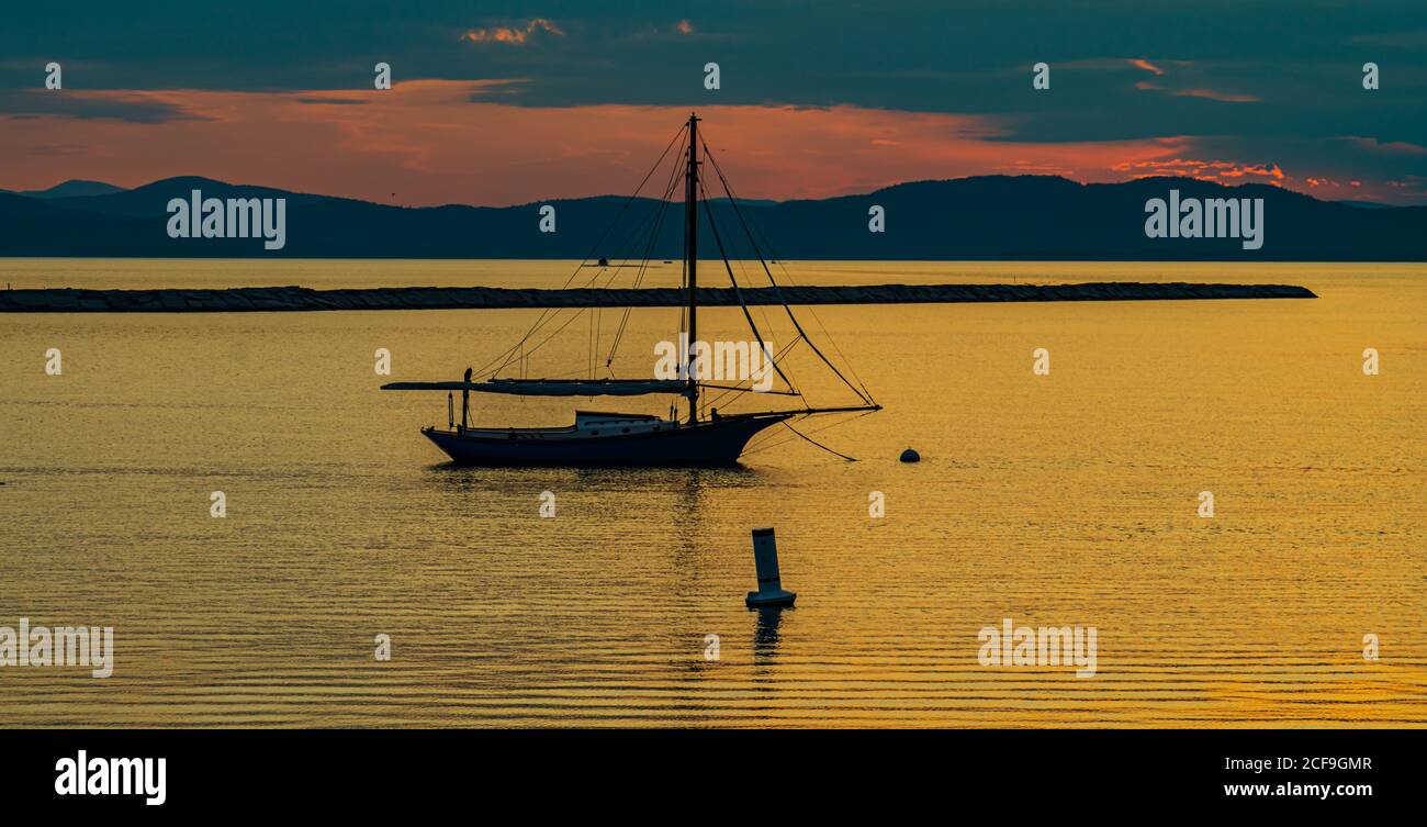 barca a vela ormeggiata sulle rive del lago Champlain in Vermont Come il tramonto dietro le montagne Adirondack a New York attraverso il lago Foto Stock