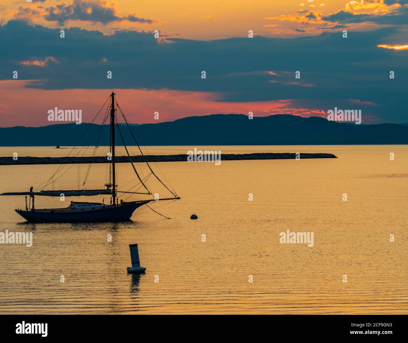 barca a vela ormeggiata sulle rive del lago Champlain in Vermont Come il tramonto dietro le montagne Adirondack a New York attraverso il lago Foto Stock