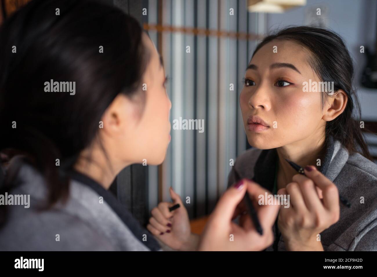 Donna asiatica applicazione eyeliner di fronte allo specchio Foto Stock