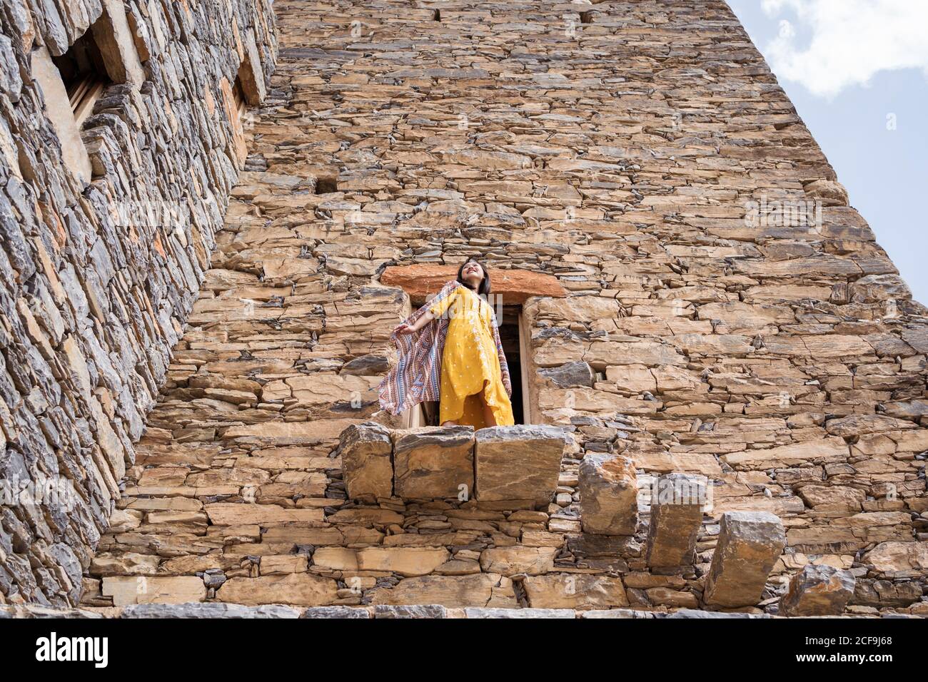 Dal basso di monumentale antico edificio con remota turista femminile uscendo dalla porta in abito giallo mentre godendo caldo Giornata di sole in Marble Village ad al Bahah Foto Stock