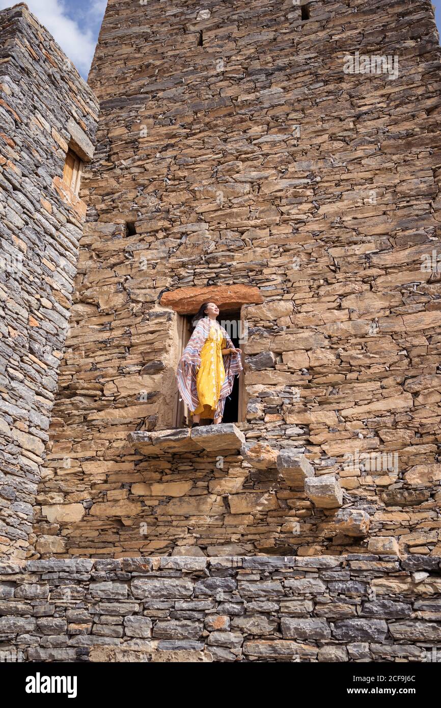 Dal basso di monumentale antico edificio con remota turista femminile uscendo dalla porta in abito giallo mentre godendo caldo Giornata di sole in Marble Village ad al Bahah Foto Stock