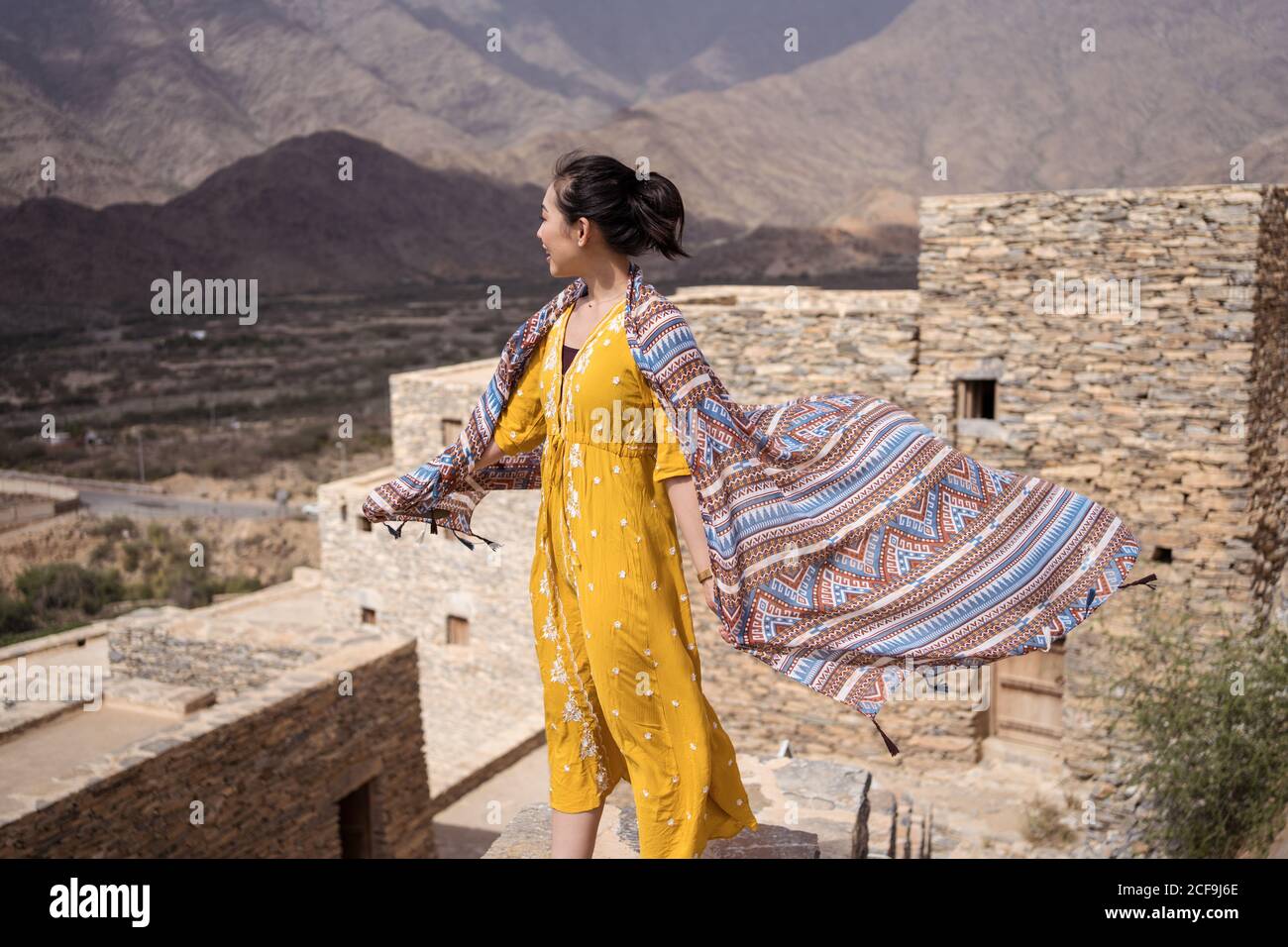 antico edificio monumentale con remota turista femminile che esce porta in abito giallo mentre ti godi una calda giornata di sole Marble Village ad al Bahah Foto Stock