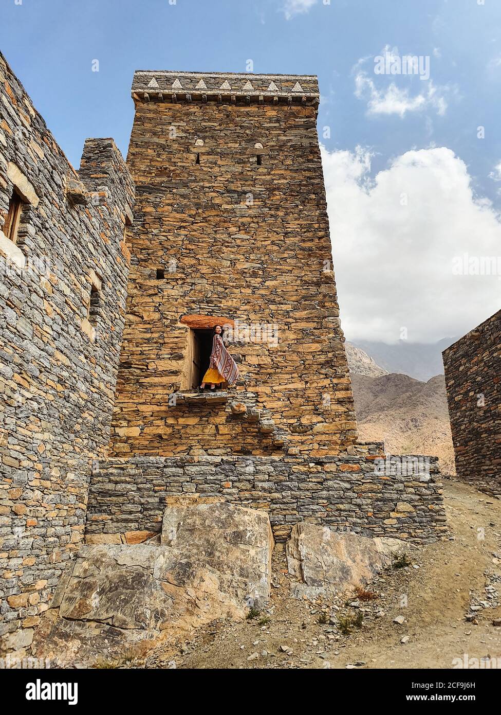 Dal basso di monumentale antico edificio con remota turista femminile uscendo dalla porta in abito giallo mentre godendo caldo Giornata di sole in Marble Village ad al Bahah Foto Stock