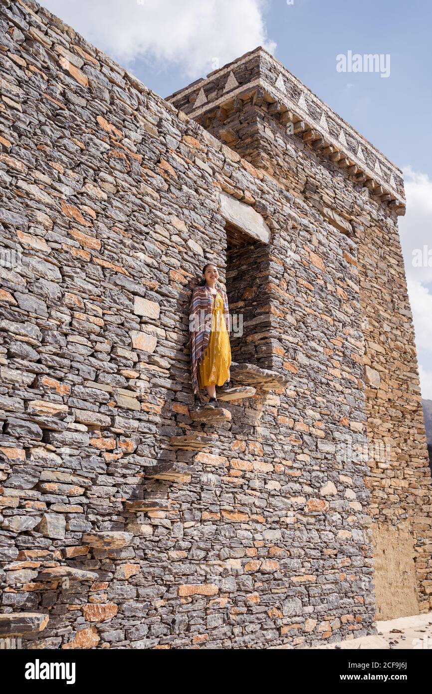 Dal basso di monumentale antico edificio con remota turista femminile uscendo dalla porta in abito giallo mentre godendo caldo Giornata di sole in Marble Village ad al Bahah Foto Stock