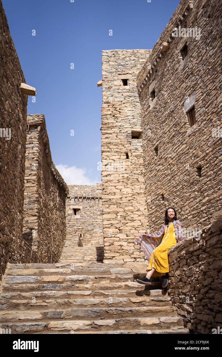 Dal basso di monumentale antico edificio con remota turista femminile uscendo dalla porta in abito giallo mentre godendo caldo Giornata di sole in Marble Village ad al Bahah Foto Stock