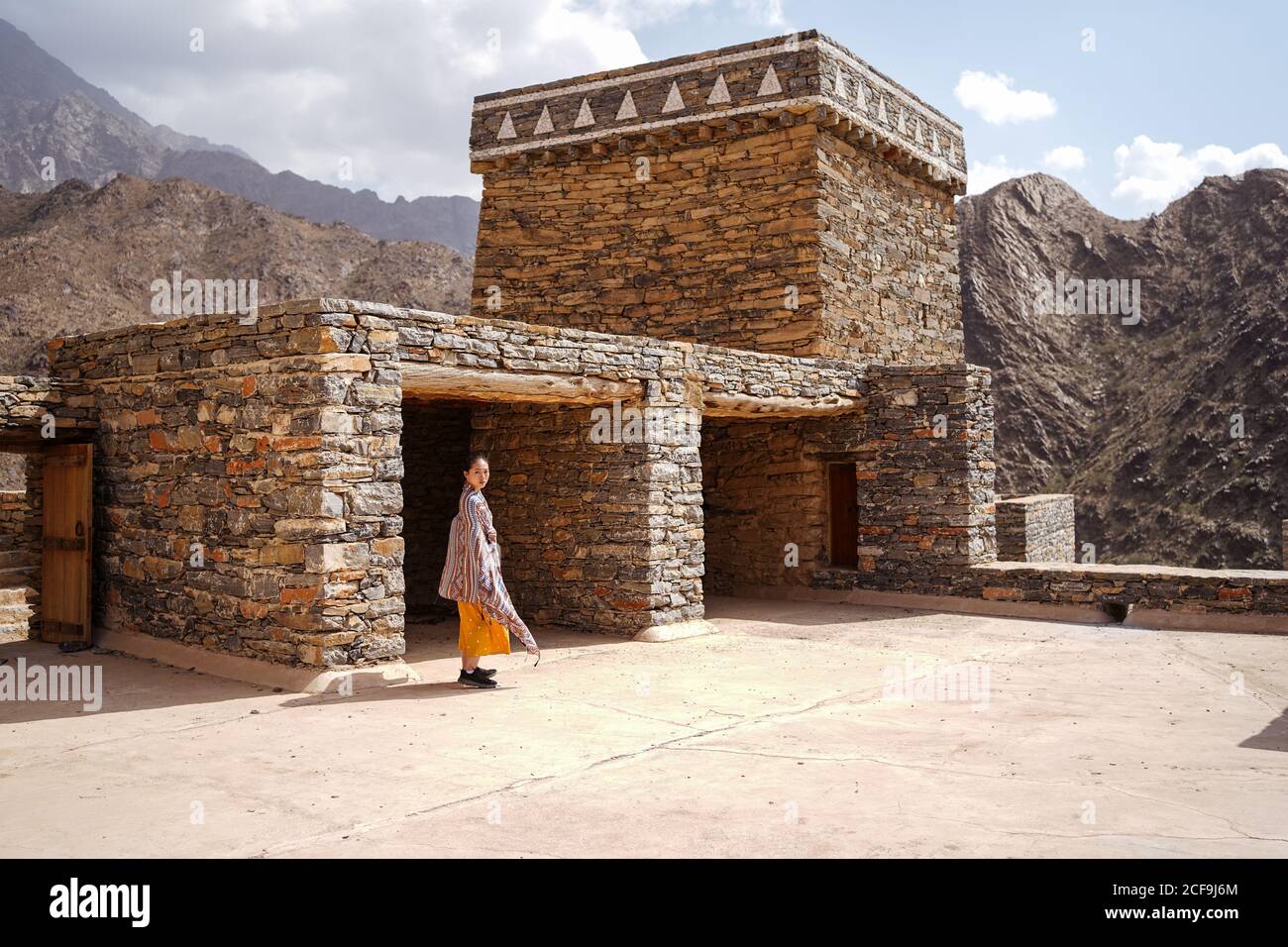 antico edificio monumentale con remota turista femminile che esce porta in abito giallo mentre ti godi una calda giornata di sole Marble Village ad al Bahah Foto Stock