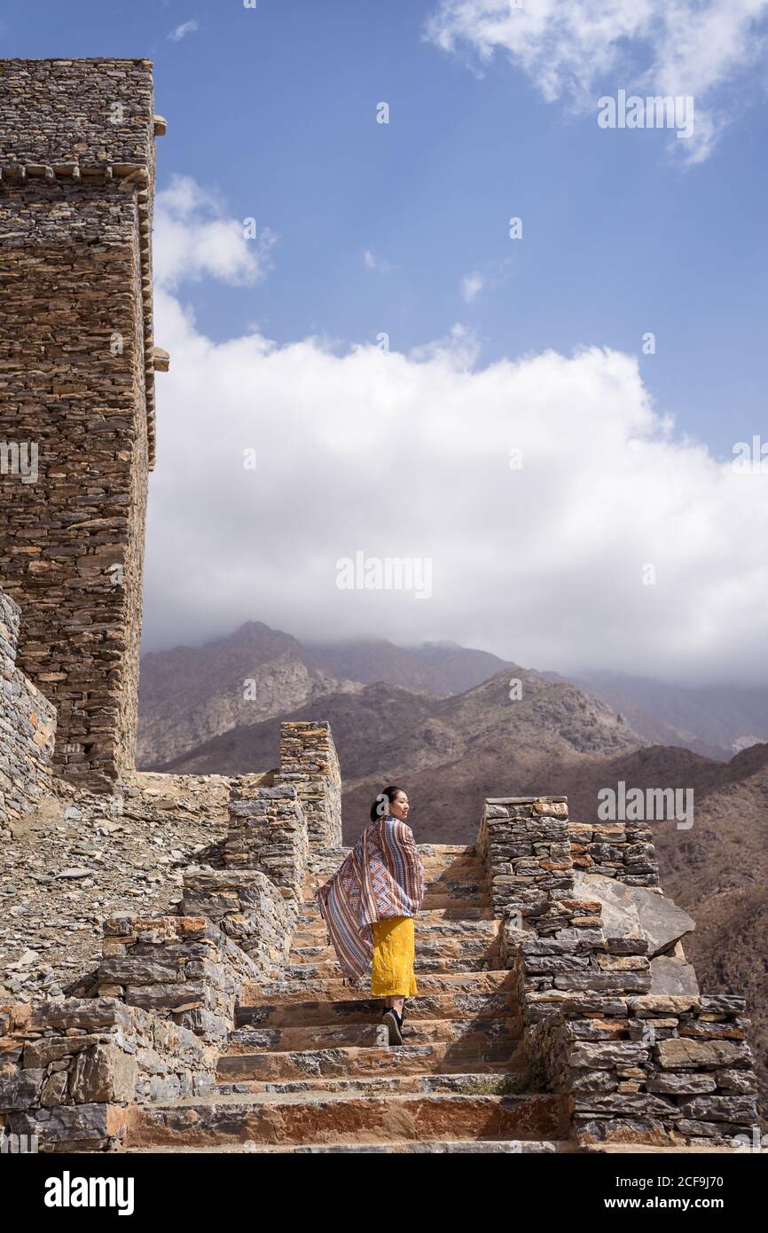 antico edificio monumentale con remota turista femminile che esce porta in abito giallo mentre ti godi una calda giornata di sole Marble Village ad al Bahah Foto Stock