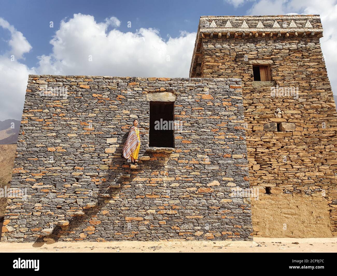 Dal basso di monumentale antico edificio con remota turista femminile uscendo dalla porta in abito giallo mentre godendo caldo Giornata di sole in Marble Village ad al Bahah Foto Stock
