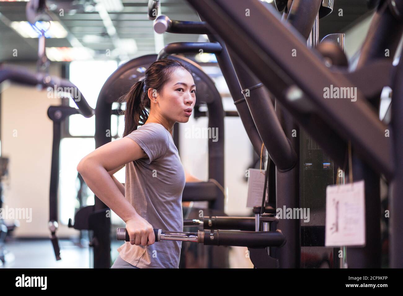 Vista laterale della giovane atleta etnica concentrata in abbigliamento sportivo facendo un'asta si tuffa sulla macchina di esercitazione mentre osservano via dentro moderno centro fitness Foto Stock