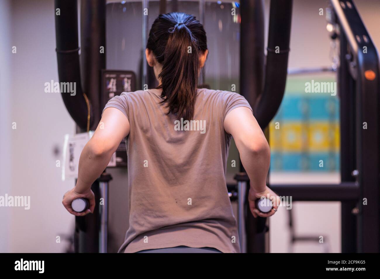 Vista posteriore della giovane atleta etnica concentrata in abbigliamento sportivo fare il bar immerge sulla macchina da ginnastica in un moderno centro fitness Foto Stock