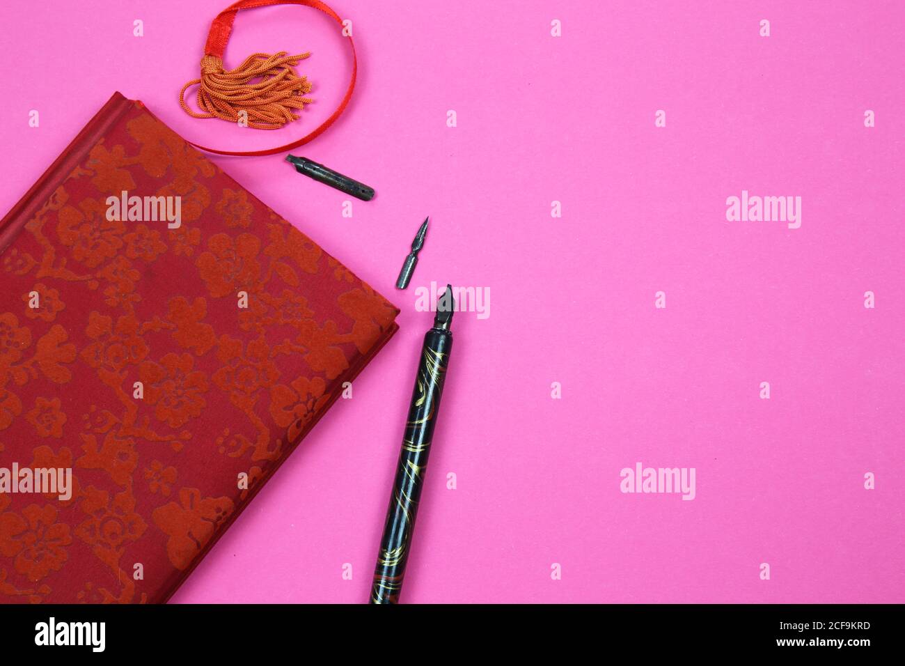 Visualizza su un notebook isolato con copertina floreale rossa, vecchia penna a inchiostro piuma e segnalibro su sfondo rosa con spazio per la copia del testo Foto Stock