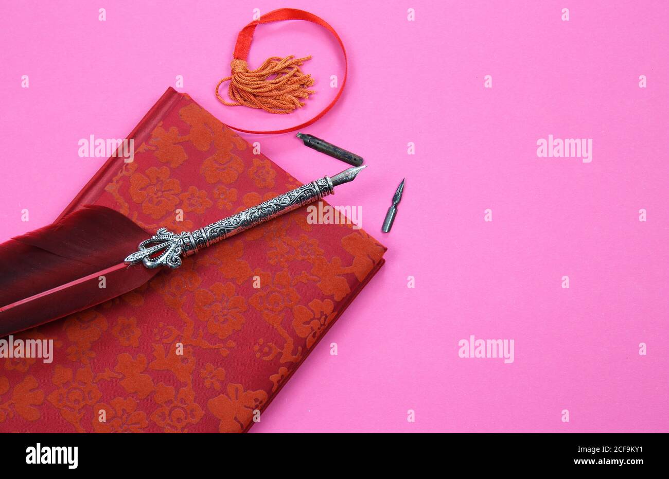 Visualizza su un notebook isolato con copertina floreale rossa, vecchia penna a inchiostro piuma e segnalibro su sfondo rosa con spazio per la copia del testo Foto Stock
