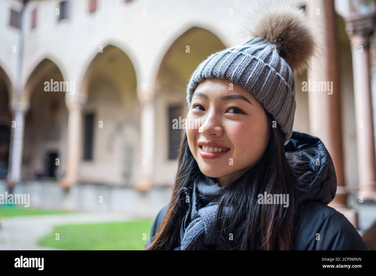 Curiosa donna asiatica di riposo in abiti caldi e cappello esplorando Bella antica Basilica di Sant Antonio di Padova guardando fotocamera Foto Stock