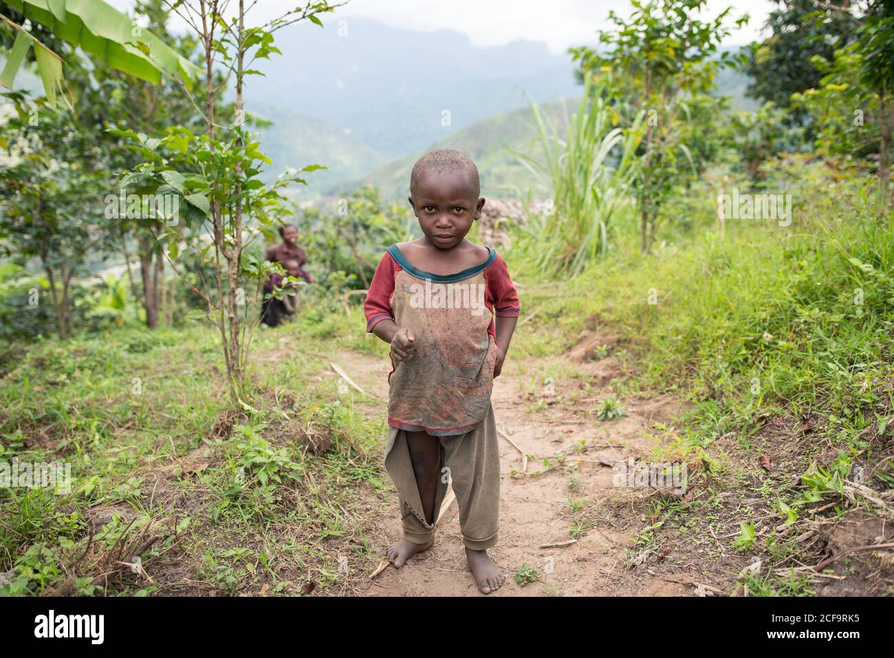 Uganda - Novembre 26 2016: Toddler africano calvo che guarda la macchina fotografica mentre cammina sulla strada sporca fuori del villaggio Foto Stock