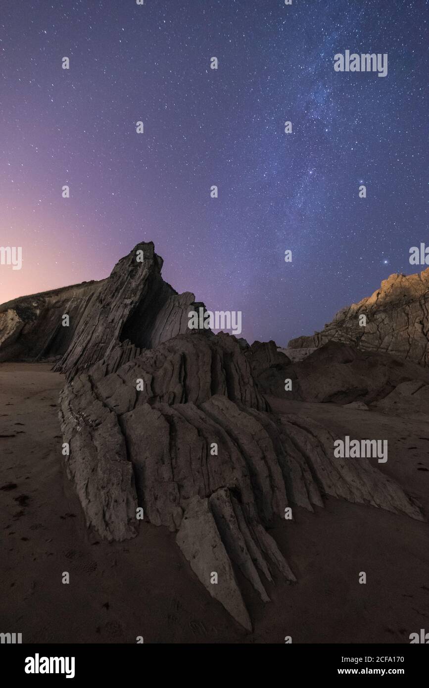 Da sotto di ruvida cima scogliera con colorata notte blu cielo e stelle lucide sullo sfondo Foto Stock