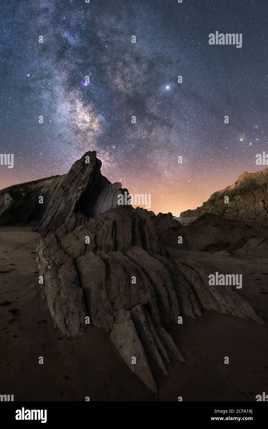 Da sotto di ruvida scogliera picco sotto modo lattiginoso colorato cielo notturno blu e stelle lucenti sullo sfondo Foto Stock