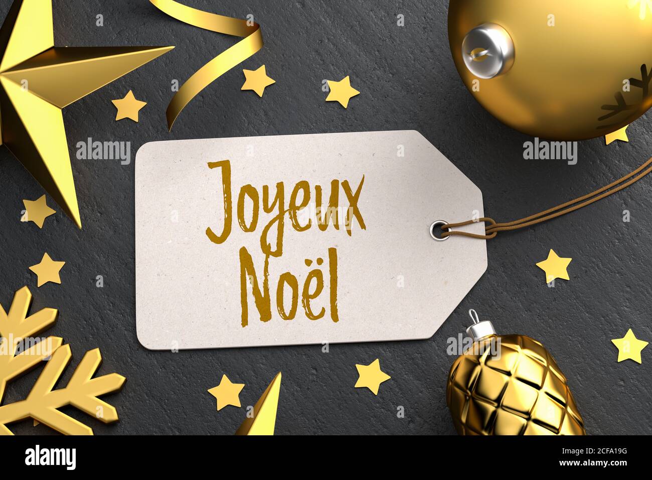 Natale - Tag regalo con il messaggio francese di Natale 'Joyeux Noël' su uno sfondo di pietra nera con ornamenti di natale color oro intorno. Foto Stock