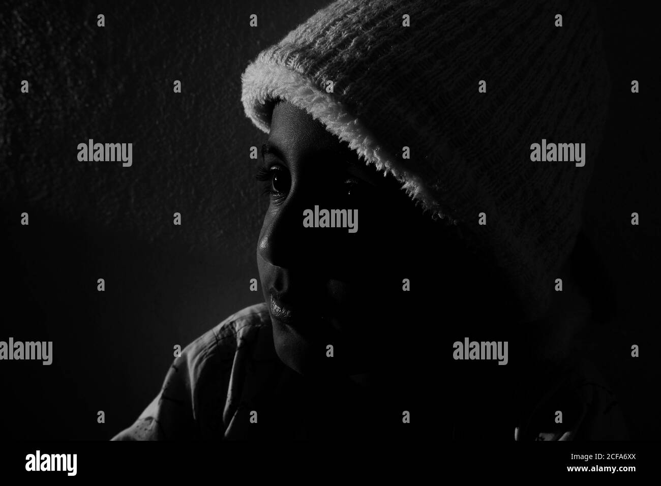Una vista laterale del ragazzo indiano con il cappuccio sotto il sole foto in bianco e nero con illuminazione Foto Stock