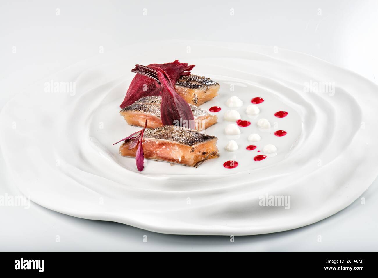 Spuntino fresco e gustoso di filetto di salmone con vivide erbe vinose su un piatto rotondo in ceramica su sfondo bianco in un ristorante moderno Foto Stock