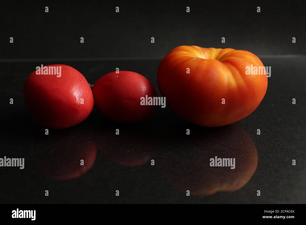 tre pomodori rossi gialle giacciono su un lato di sfondo nero visualizzare lo sfondo degli alimenti con lo spazio per la copia Foto Stock