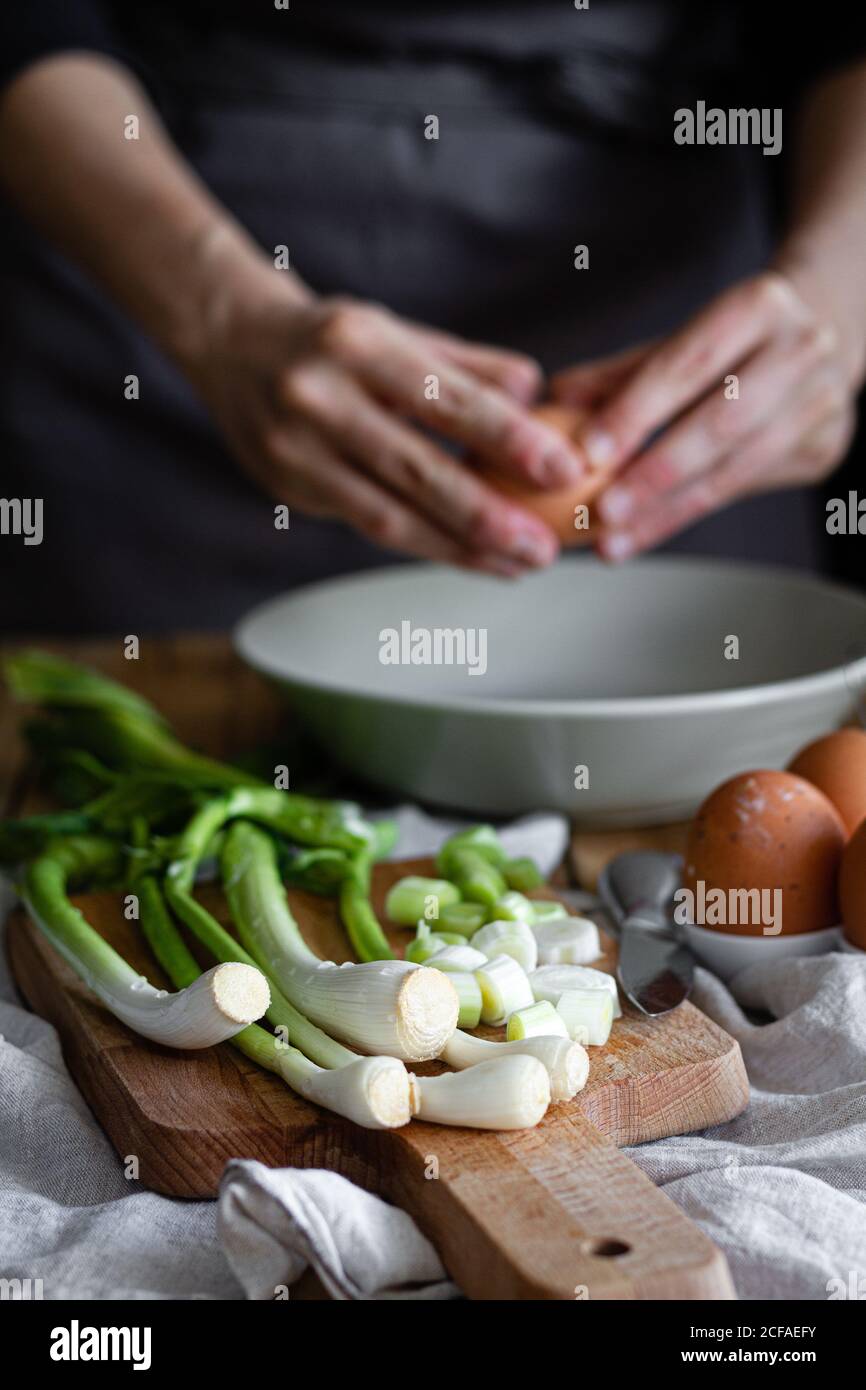 Cropped Woman mani rompere uova in una ciotola con un mazzo di capesante fresche e funghi posti sul tagliere vicino a semi di papavero Foto Stock