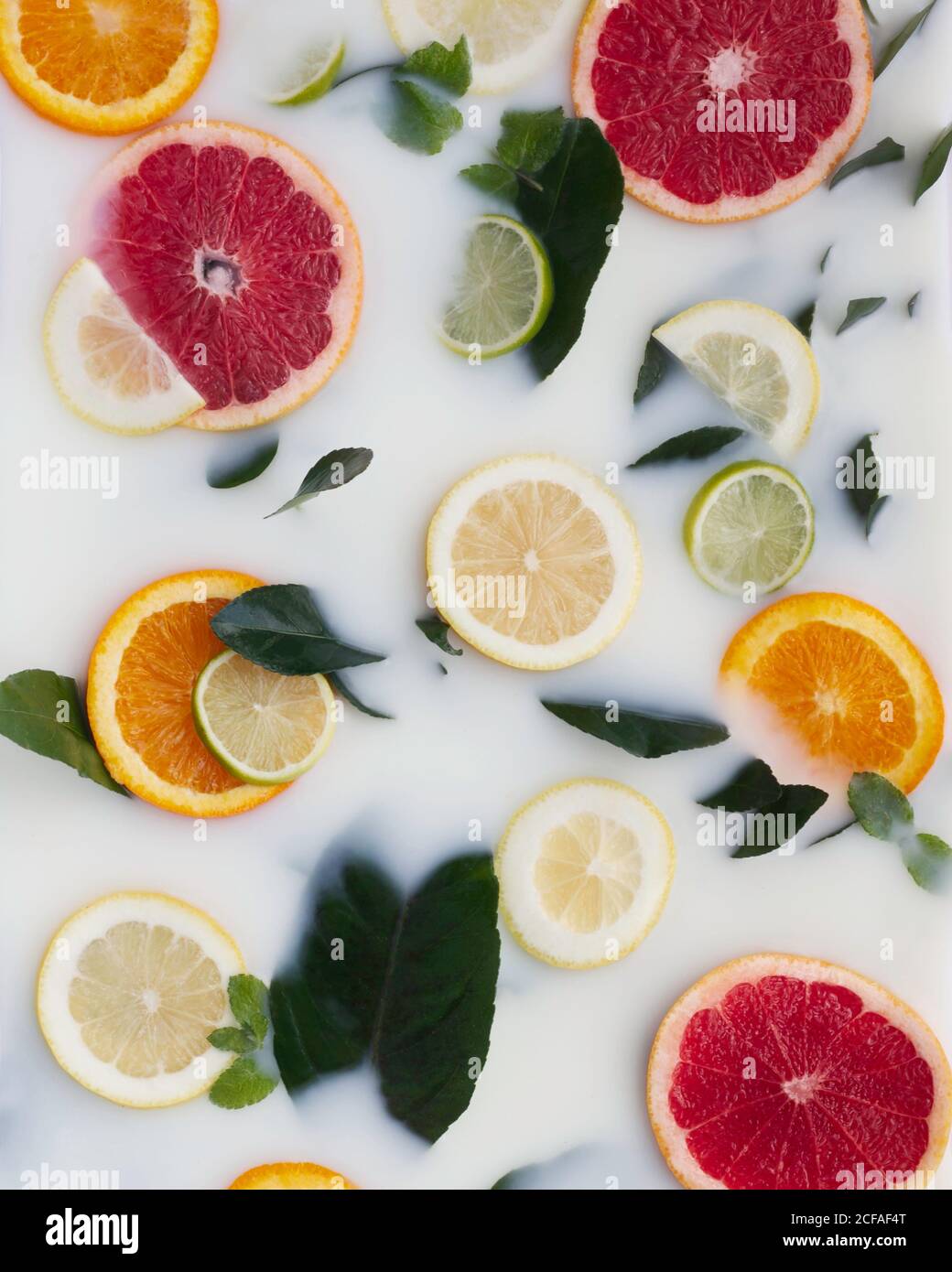 Vista dall'alto di colorati segmenti di pompelmo di lime arancio decorata con foglie verdi e tubi in plastica in liquido bianco Foto Stock