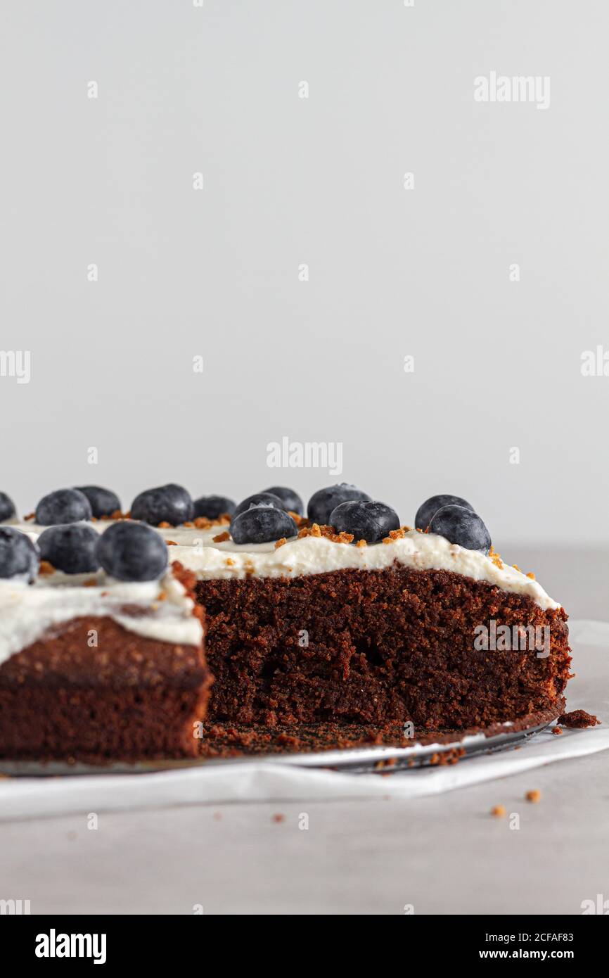 Fetta di pan di Spagna di cioccolato fatto in casa con panna montata fresca panna e mirtilli interi posti sul tavolo in cucina leggera Foto Stock