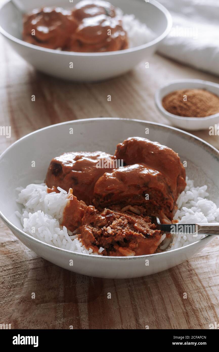 Dall'alto ciotole di riso e deliziose polpette di lenticchie con salsa di curry posta vicino alle spezie e al tovagliolo su un tavolo di legno a casa Foto Stock