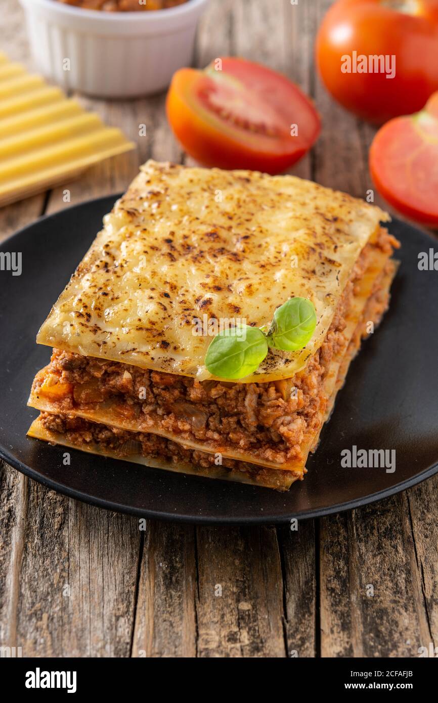 Pezzo di lasagne di carne su piastra nera su tavolo di legno Foto Stock