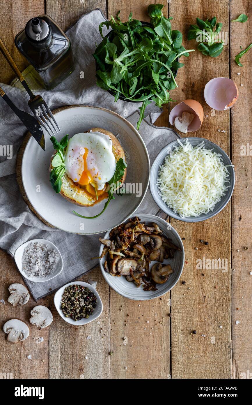 Vista dall'alto uovo fritto sulla patata su un tavolo di legno con funghi fritti formaggio grattugiato ed erbe Foto Stock