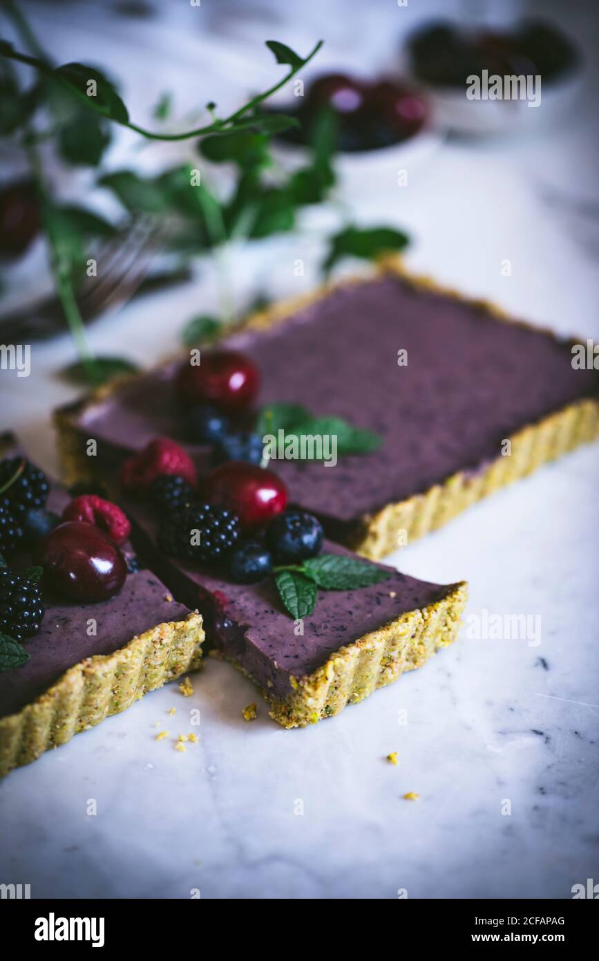 Dall'alto maturi gustosi ciliegia mora lampone di mirtillo con verde gambi sulla cima di appetitosa torta rettangolare su tavola bianca Foto Stock