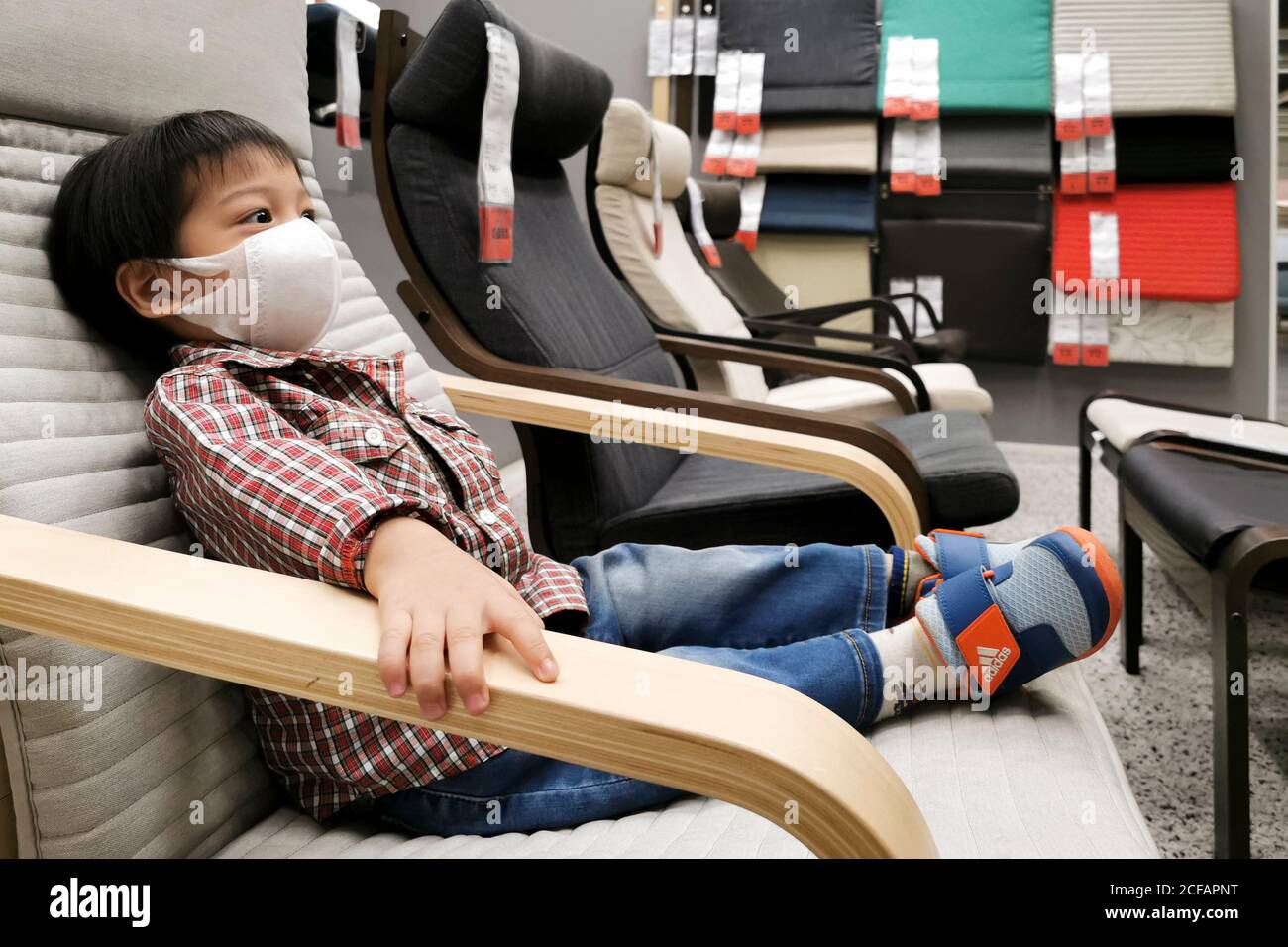 Bangkok, Thailandia - 4 settembre 2020 : asian boy che indossa la maschera facciale per proteggere il coronavirus o covid-19 pandemia siede in poltrona in attesa dei genitori s. Foto Stock
