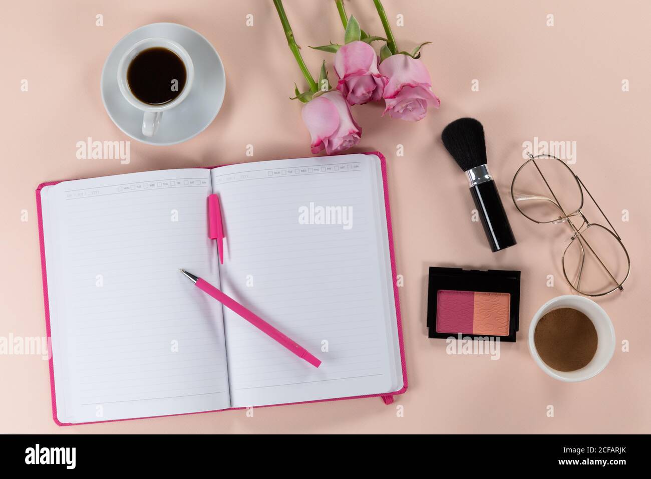 Make up vista con fiori rosa, notebook, tazza di caffè e bicchieri su sfondo rosa Foto Stock