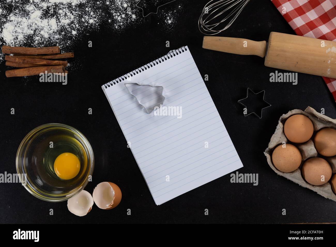 Vista di una pagina vuota del notebook con ingredienti preparati per cuocere i biscotti, disposti su una bla semplice Foto Stock