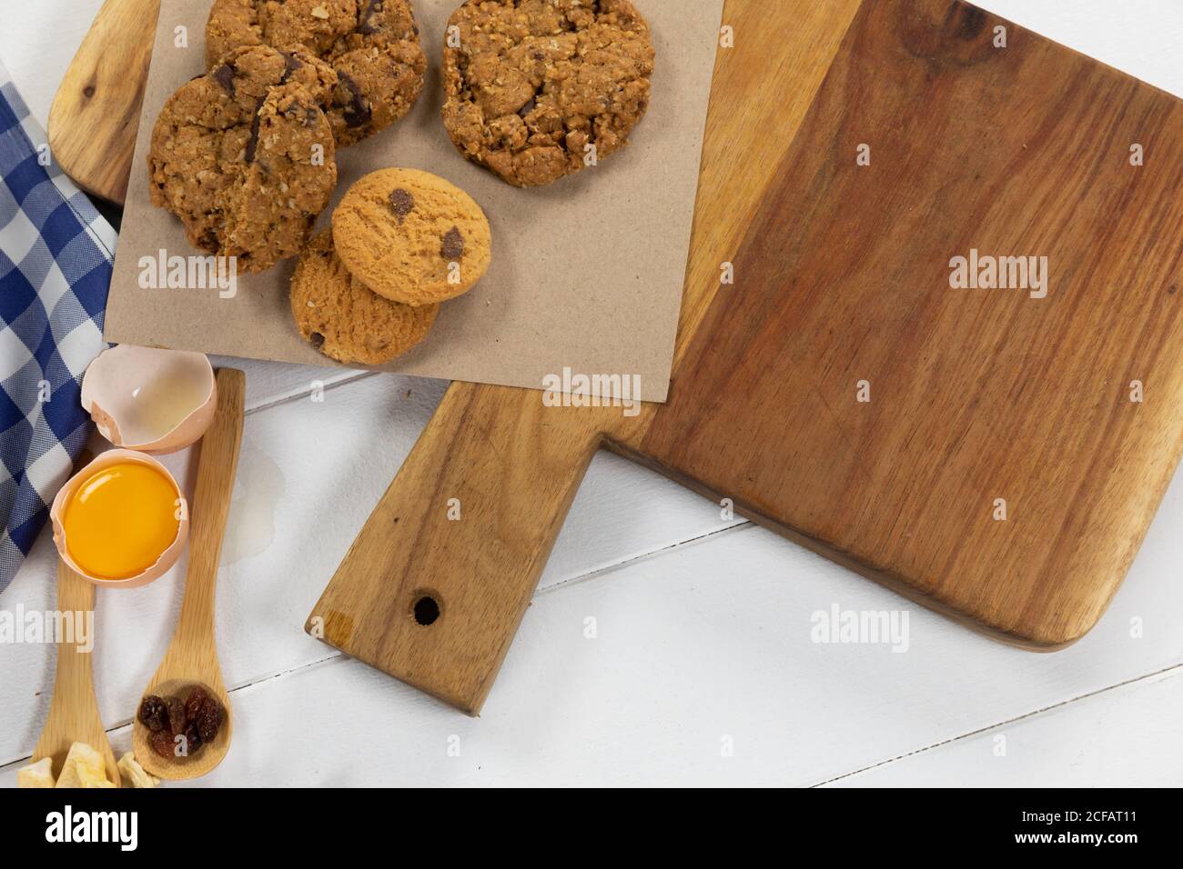 Vista di biscotti, cucchiai di frutta secca e uova su superficie di legno bianco con tovaglia Foto Stock