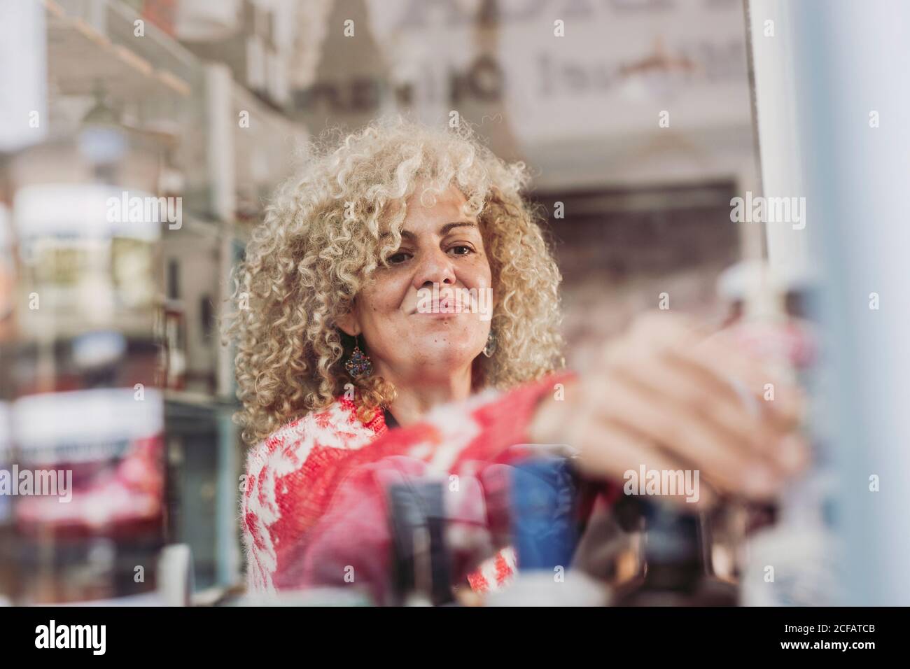 Donna adulta felice con capelli ricci che vendono formaggio nel negozio di gastronomia locale Foto Stock