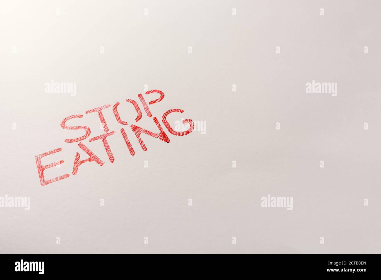 Alto angolo di testo rosso dello slogan motivazionale che dice Stop mangiare per non consumare più di quanto necessario scritto su bianco sfondo Foto Stock