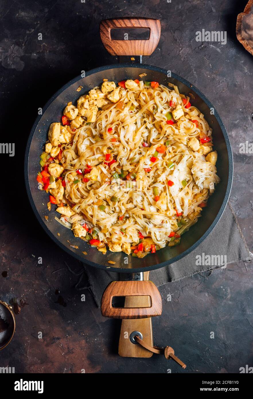 Vista dall'alto degli appetitosi spaghetti piccanti con pollo carne e verdure su padella posta su rustico scuro tabella Foto Stock