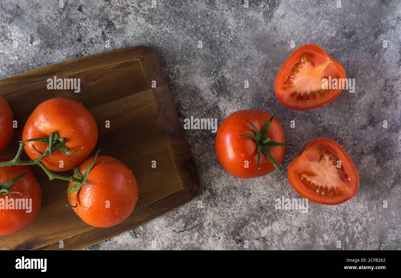 Pomodori freschi tagliati a metà e interi messi a tavola su grezzo tavolo grigio durante la preparazione del cibo in cucina Foto Stock