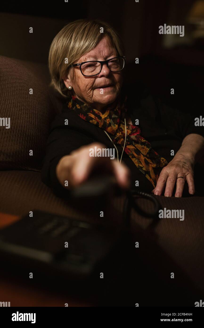 Signora anziana che risponde alla chiamata mentre si siede in camera buia in serata a casa Foto Stock