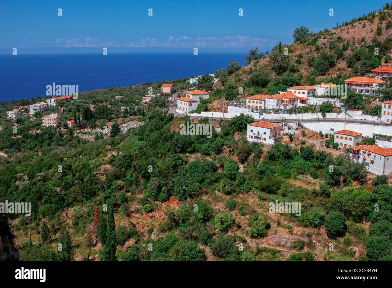 Vista del villaggio in Albania - tradizionali case bianche con tetti arancioni e persiane in legno su finestre - sulla collina di montagna, cielo blu e mare su Foto Stock