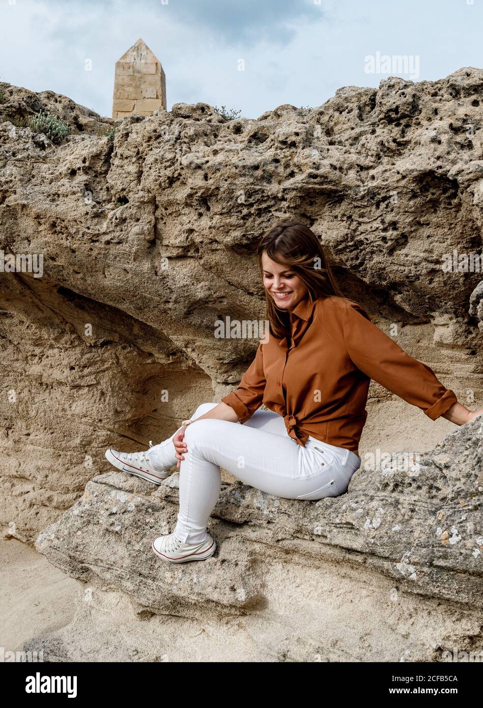 Vista laterale di Happy Beautiful Woman in jeans bianchi seduti su pietre rocciose nel deserto Foto Stock