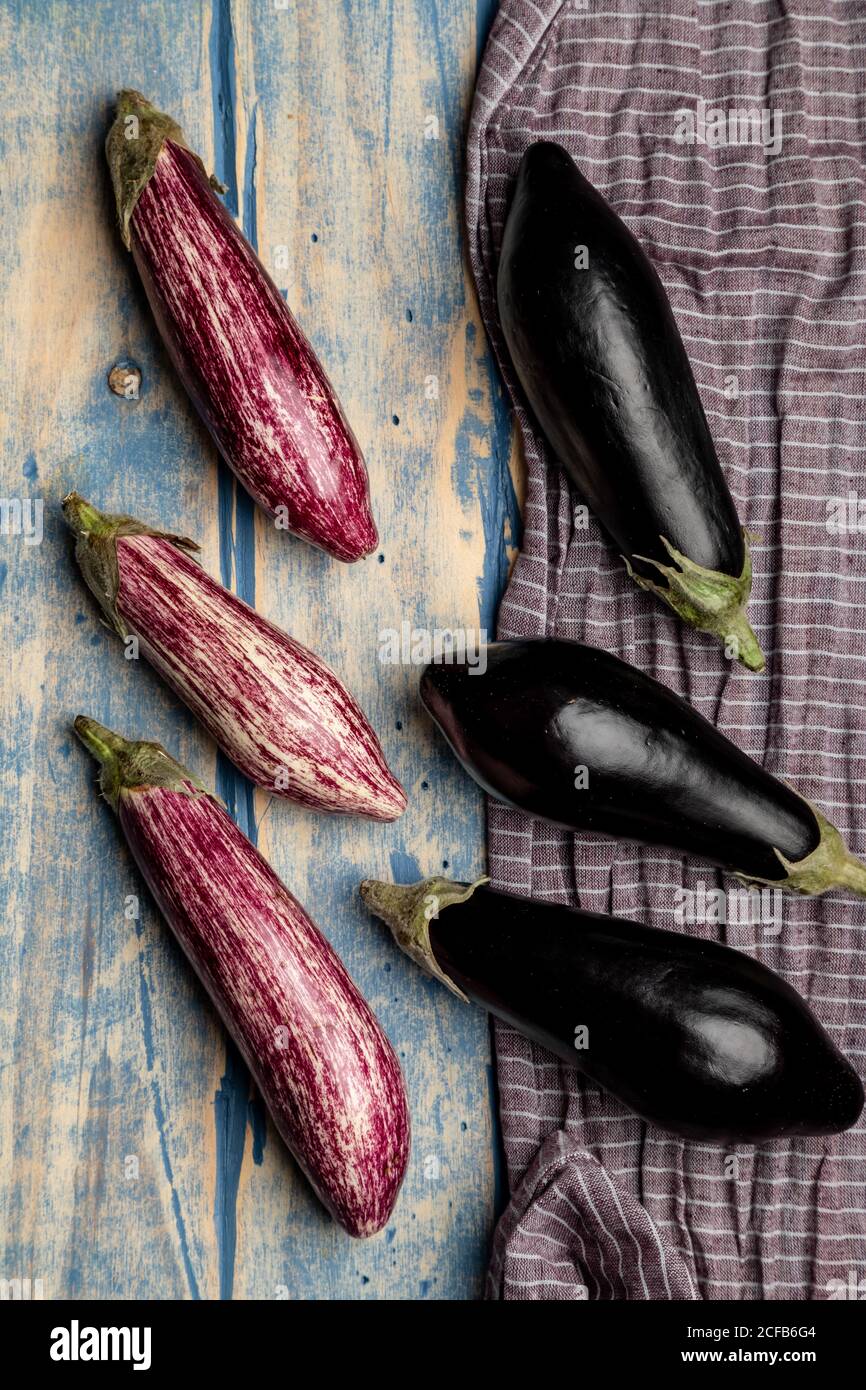 Set di melanzane fresche mature poste vicino a pezzo di striped panno su un piano di lavoro in legno resistente alle intemperie Foto Stock